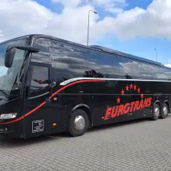 Czarny autokar firmy Eurotrans z czerwonymi pasami i gwiazdami na tle błękitnego nieba.