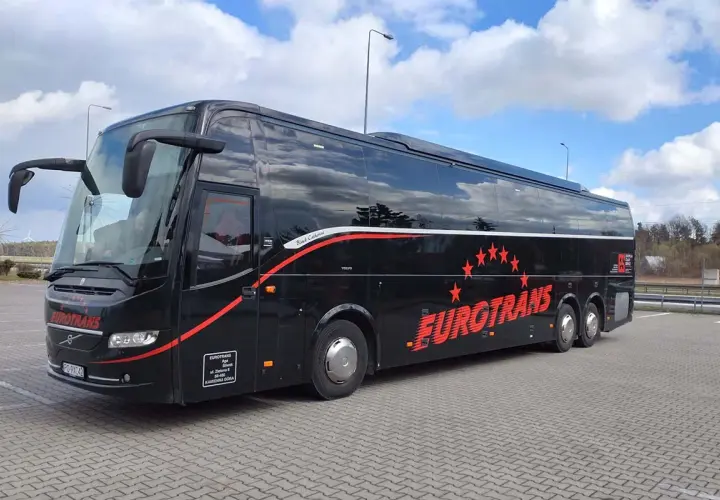 Czarny autokar firmy Eurotrans z czerwonymi pasami i gwiazdami na tle błękitnego nieba.