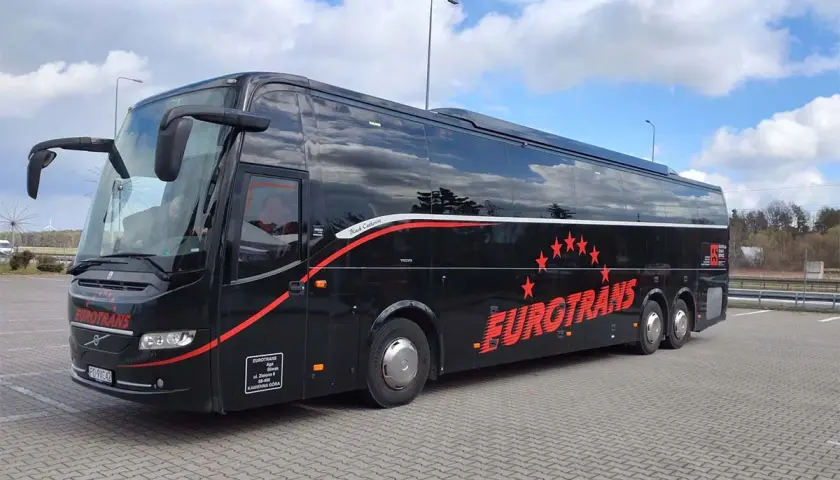 Czarny autokar firmy Eurotrans z czerwonymi pasami i gwiazdami na tle błękitnego nieba.